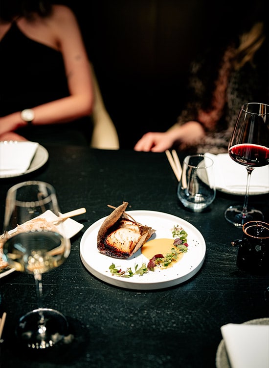 Plato de alta cocina con pescado emplatado y copas de vino tinto en un restaurante en Barcelona