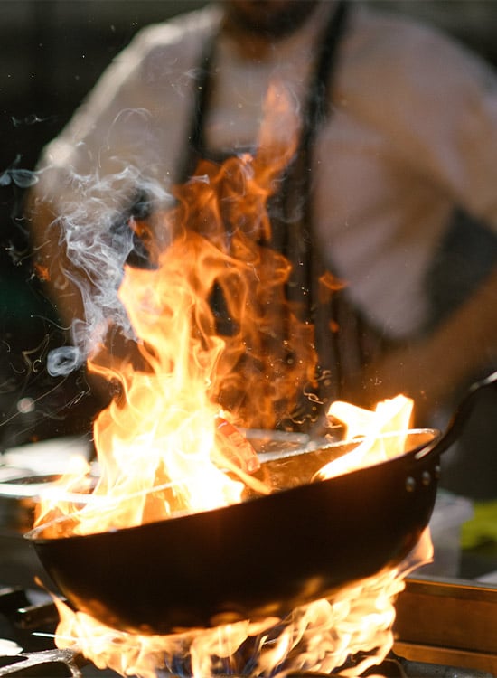 Cocinero flambeando en un wok con llamas en la cocina de un restaurante en Madrid