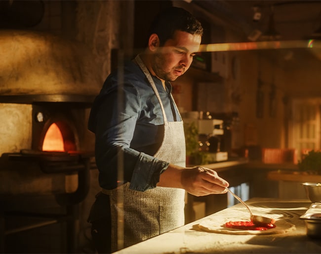 Cocinero preparando una pizza junto a un horno de leña en la cocina de un restaurante